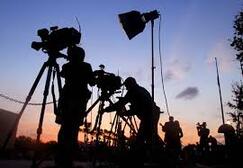 silhouetted movie crew with movie cameras and lighting equipment against sunset sky