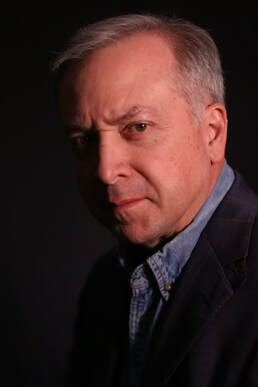 PORTRAIT PHOTO OF STAN LEWIS, WRITER IN HALF-LIGHT, FURROWED BROW, WEARING BLUE CHAMBRAY SHIRT AND DARK SPORT COAT, DRAMATIC POSE
